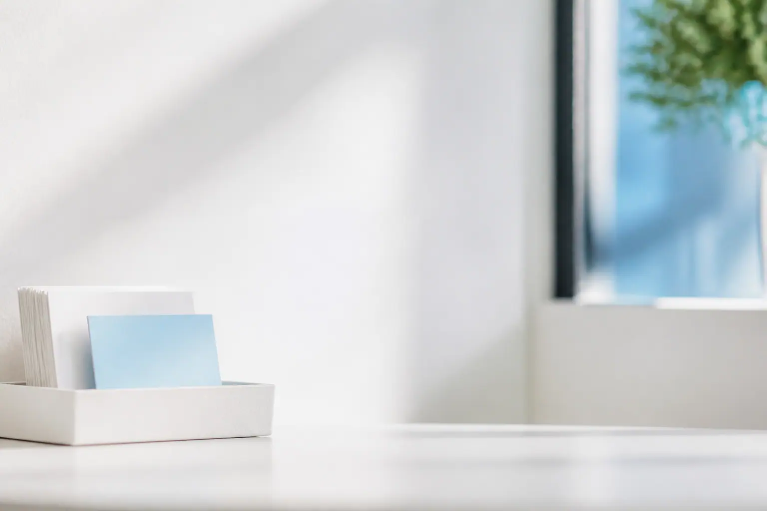 A white desk tray of blank cards, one pale-blue card set forward, by a sunlit window.