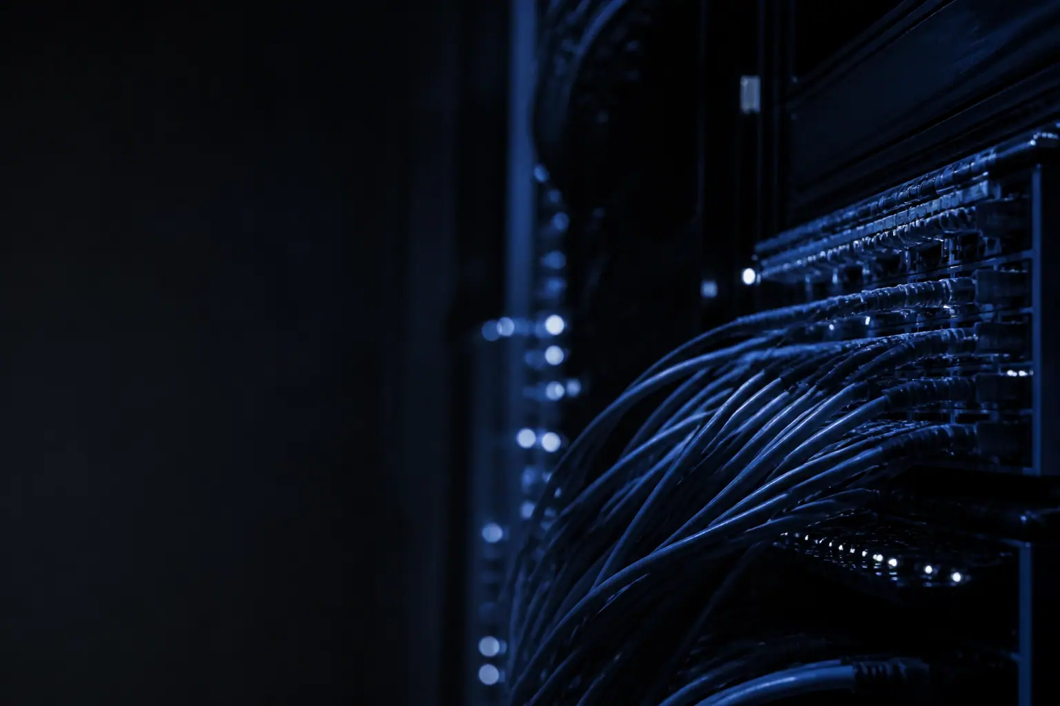 Cold-lit network switching equipment in a dark rack, fibre runs fanning out of frame.