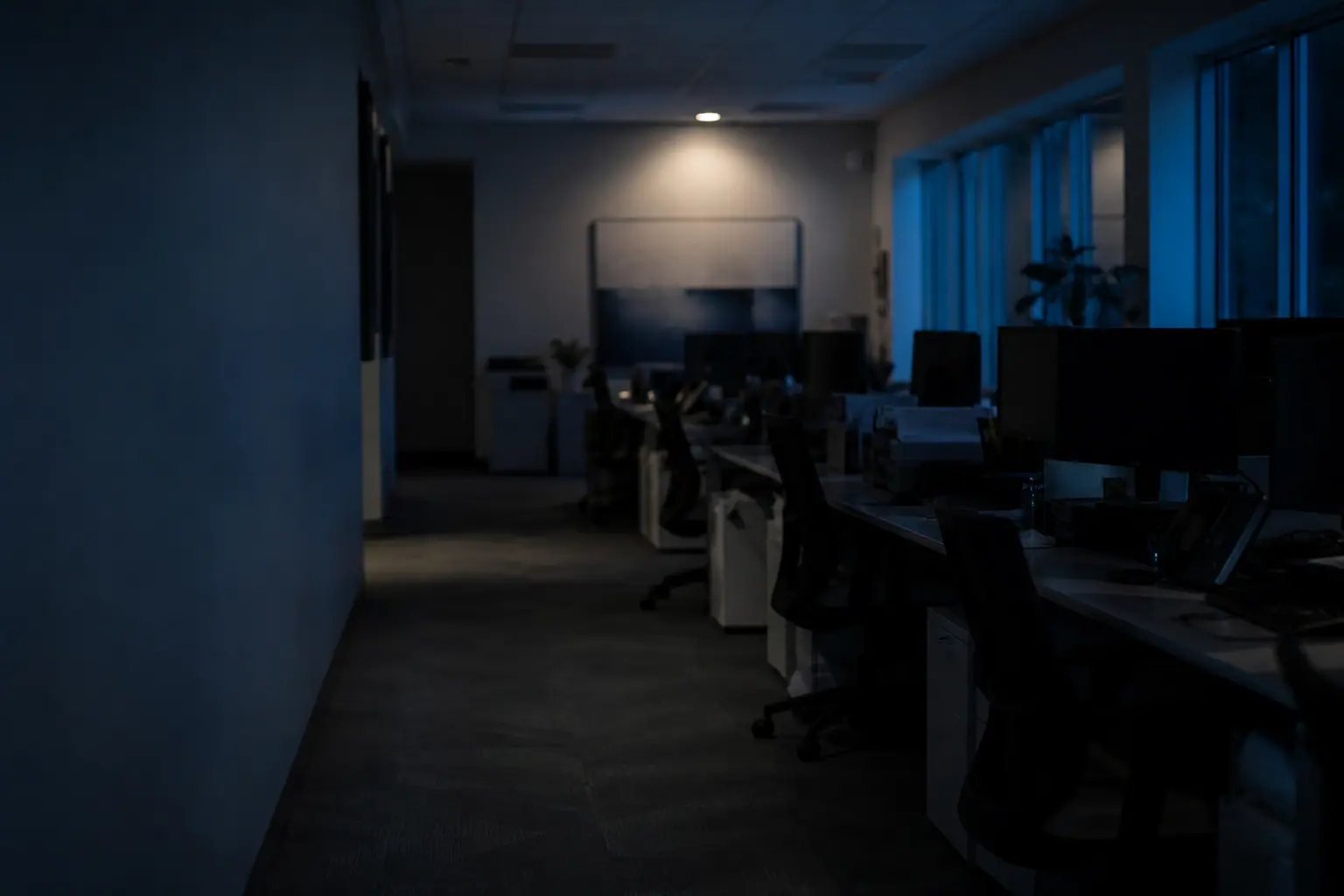 An empty hospital billing office at night, lit only by the glow of a row of dormant workstations.